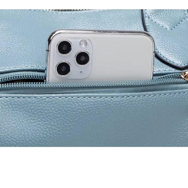 Smartphone bianco con tripla fotocamera in una tasca di borsa in pelle azzurra. Accessori moda, tecnologia, design elegante.
