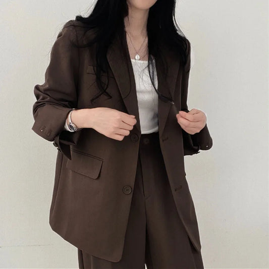 Donna in blazer marrone elegante, abbinato a pantaloni coordinati e top bianco. Moda femminile, abbigliamento formale, stile business casual.