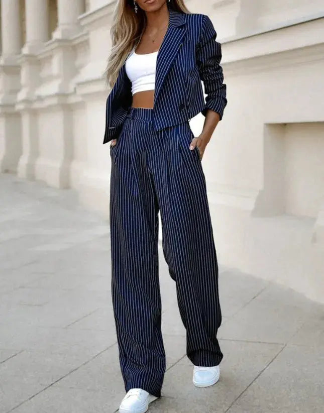 Completo donna a righe blu e nere, giacca e pantaloni larghi, top bianco corto, scarpe da ginnastica bianche, moda casual elegante.
