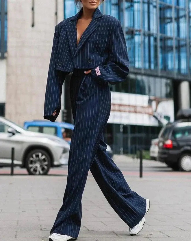 Donna con completo giacca e pantaloni a righe blu, stile elegante, scarpe bianche, sfondo urbano. Moda femminile, abbigliamento formale.