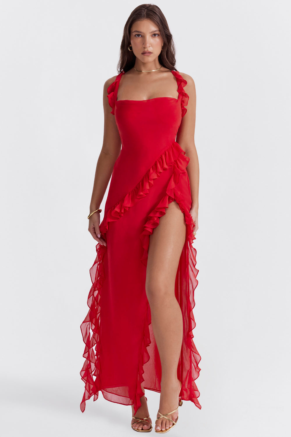 Abito lungo rosso con volant, spacco alto e spalline, indossato da una donna. Elegante e moderno, ideale per eventi serali e cerimonie.
