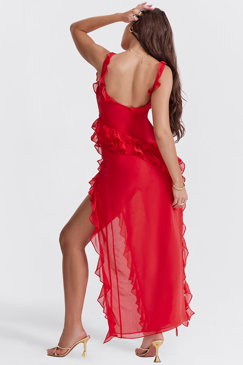 Abito lungo rosso con volant, spacco laterale, indossato da donna di spalle. Elegante e moderno, perfetto per serate e occasioni speciali.